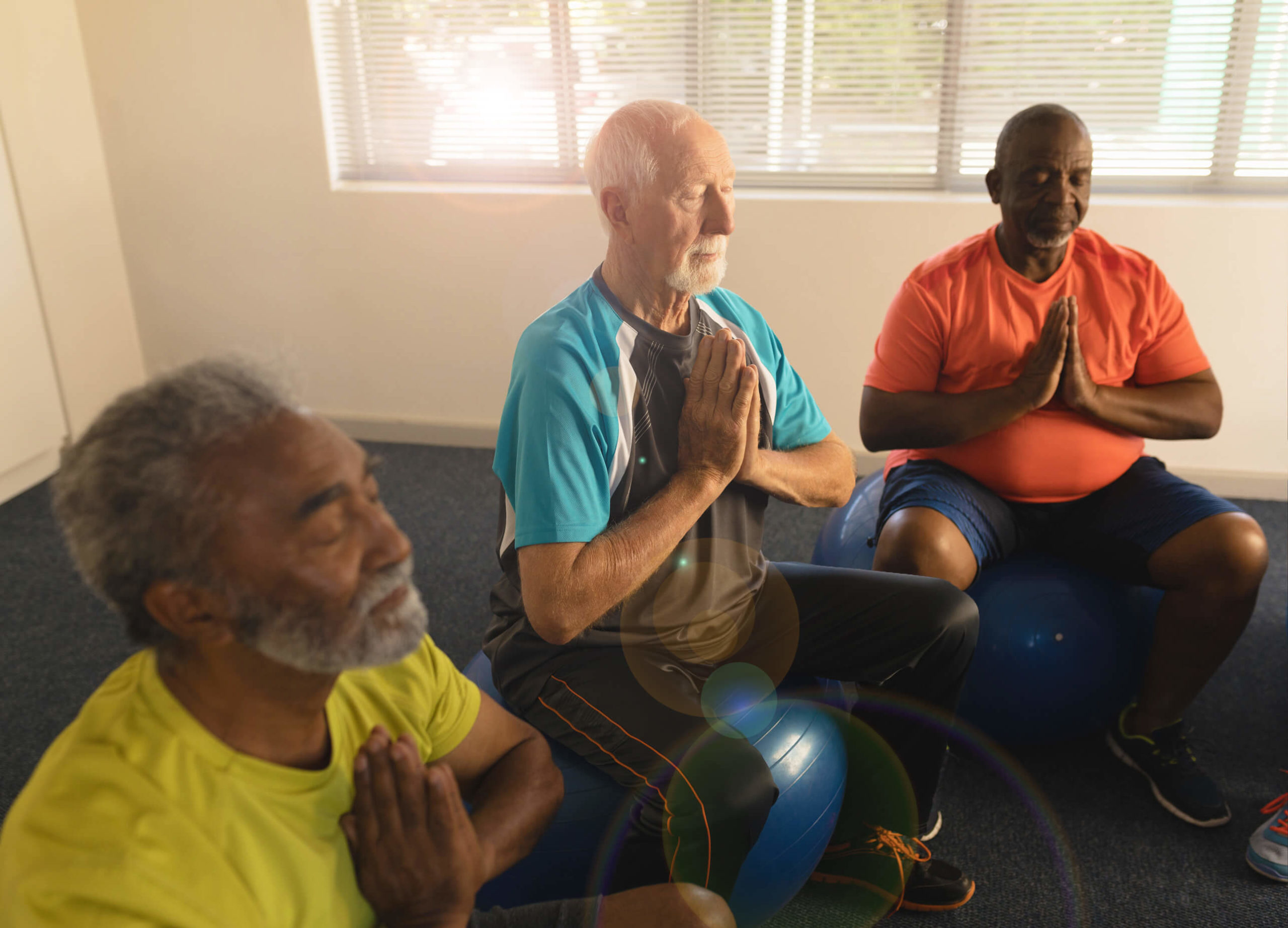 Three residents sitting on exercise balls in a peaceful meditative pose with closed eyes.