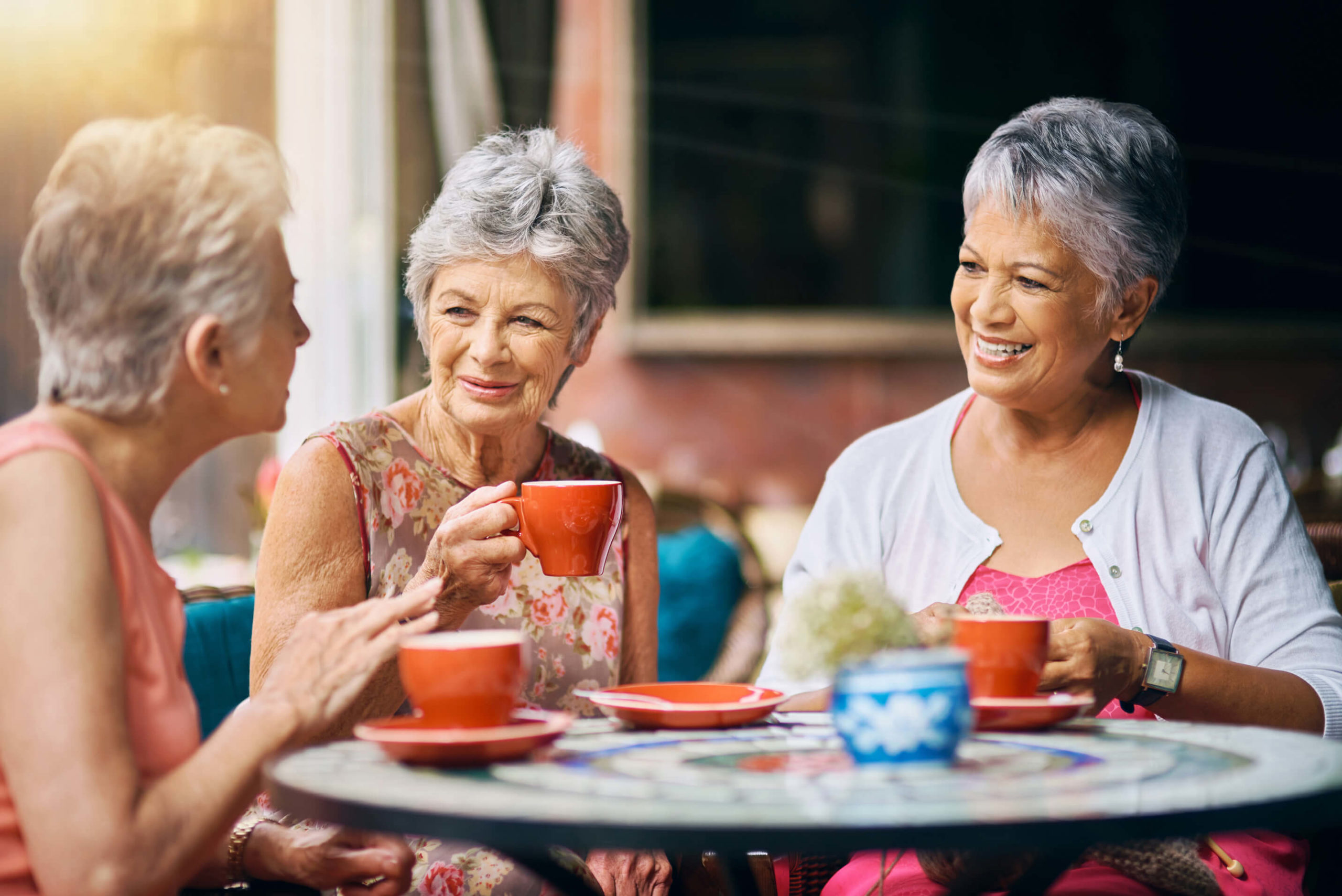 Elderly residents socializing at a table, holding colorful tea cups while engaged in conversation.