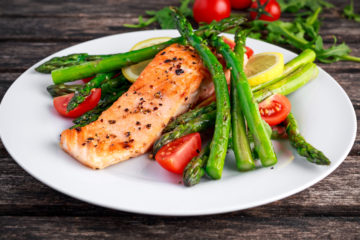 Salmon with asparagus, tomatoes, lemon, on white plate